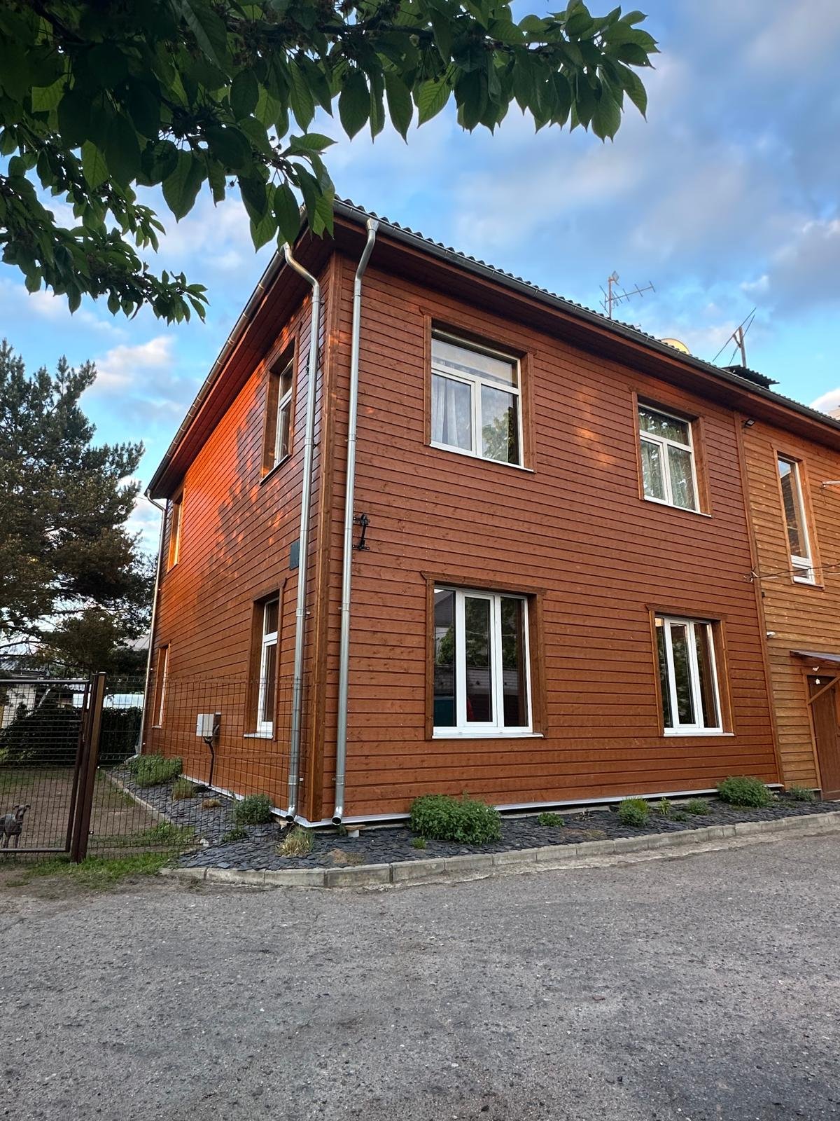 Renovuotas dviejų aukštų namas su rusvos spalvos horizontalių medžio lentų fasadu